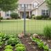 Wildlife-friendly mesh fencing along the base of a residential garden, with a small rabbit and box turtle near an open lower gap in the fence.