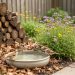 A compact courtyard garden with native wildflowers, a log pile for wildlife shelter, and a shallow water dish attracting birds and pollinators.
